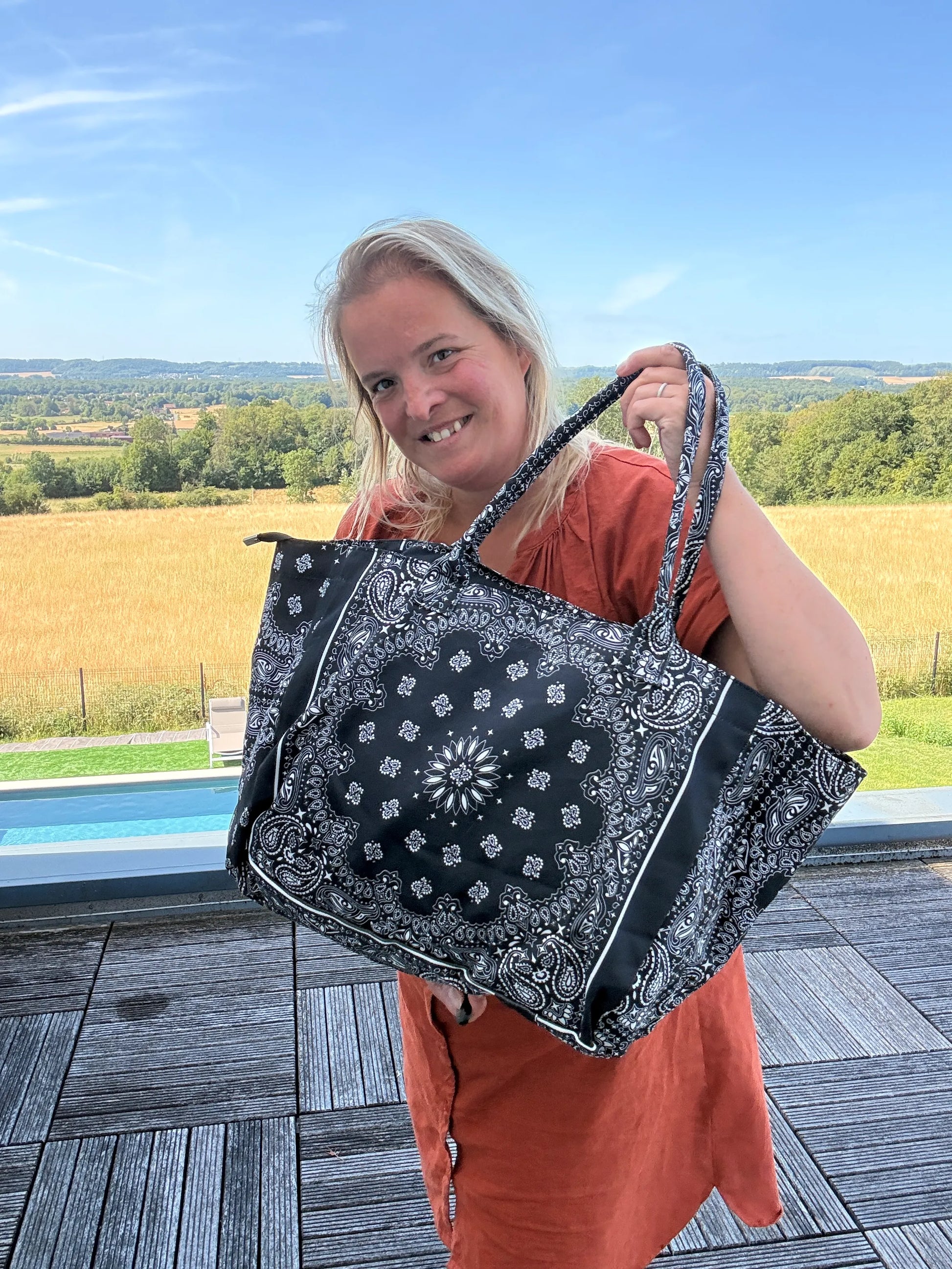 Sac polochon épaule en coton noir avec motif paisley, femme tenant le grand sac zippé à l’épaule sur une terrasse en plein air.