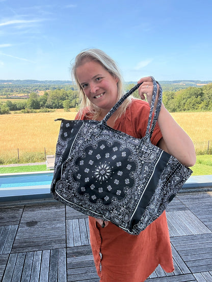 Sac polochon épaule en coton noir avec motif paisley, femme tenant le grand sac zippé à l’épaule sur une terrasse en plein air.