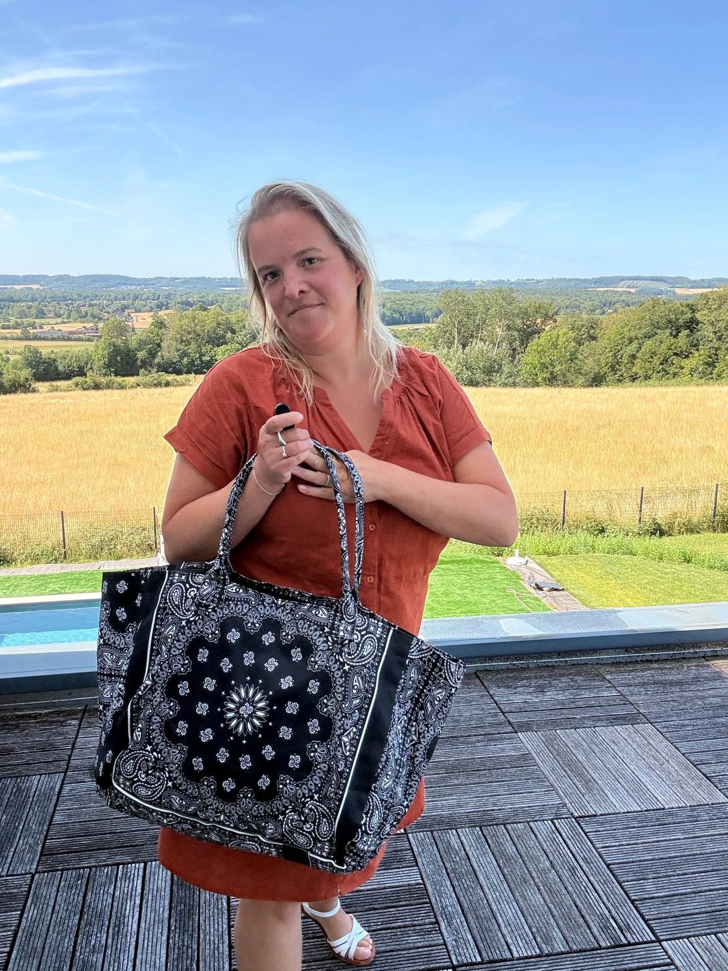 Sac polochon épaule coton paisley noir en grand format zippé, porté par une femme devant un paysage champêtre.