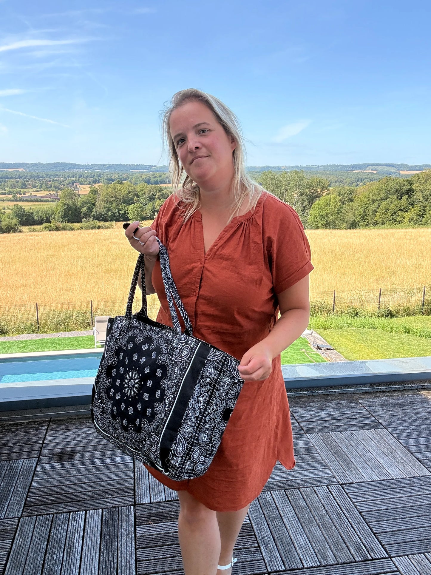 Sac polochon épaule coton Paisley noir grand format zippé, porté par une femme en robe orange dehors près d’une piscine.