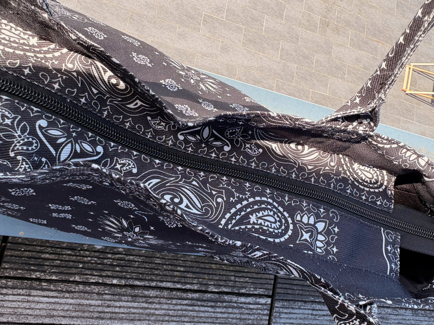 Sac polochon noir imprimé paisley en coton avec fermeture éclair visible sur le dessus.