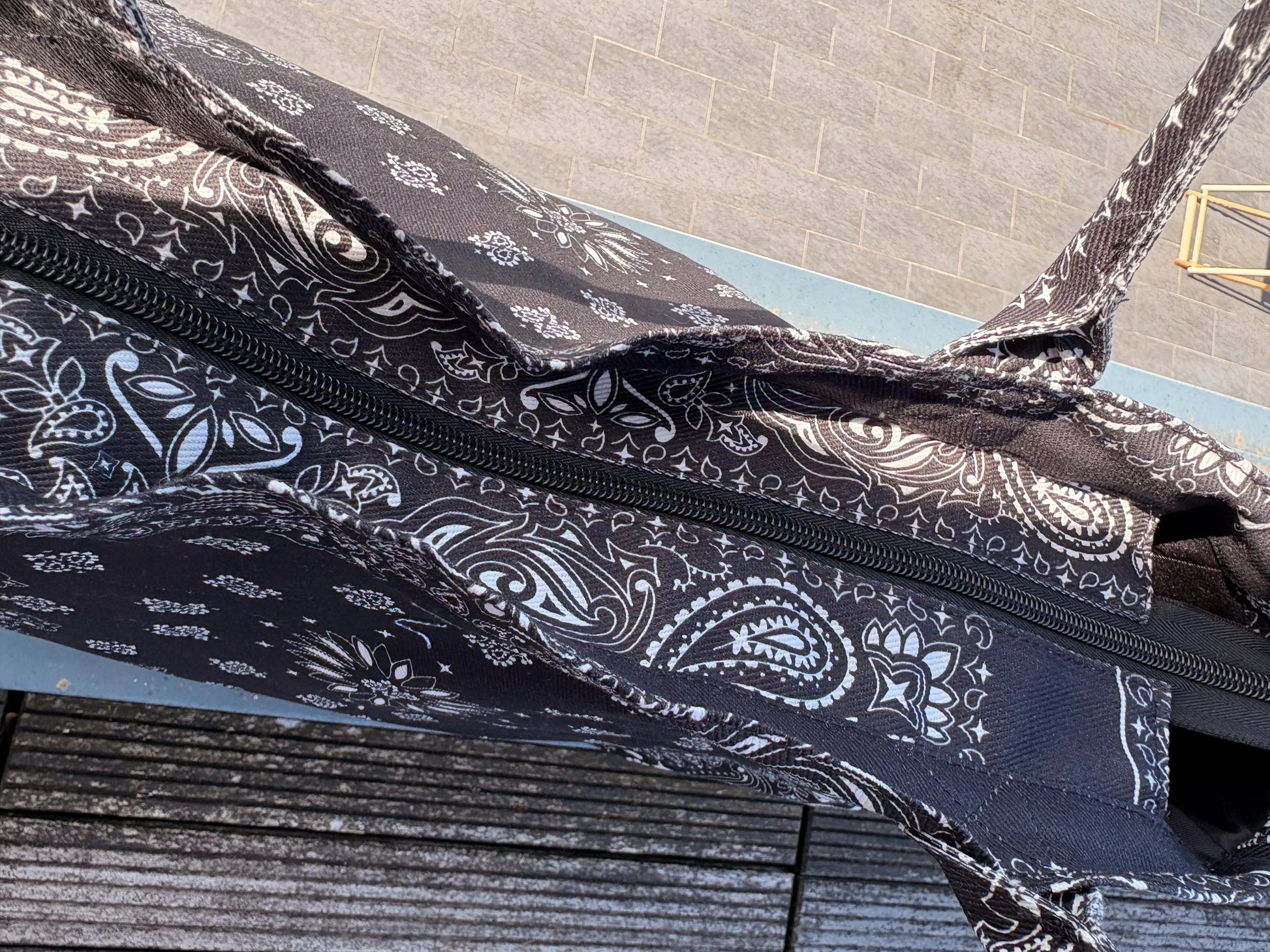 Sac polochon noir imprimé paisley en coton avec fermeture éclair visible sur le dessus.