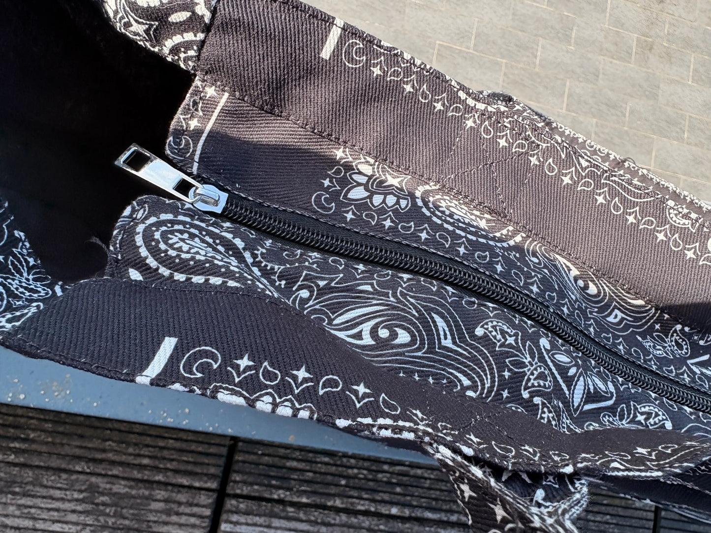 Sac polochon noir et blanc avec motif paisley, fermeture éclair zippée et détails coton, vue sur la bandoulière et le bord du sac.