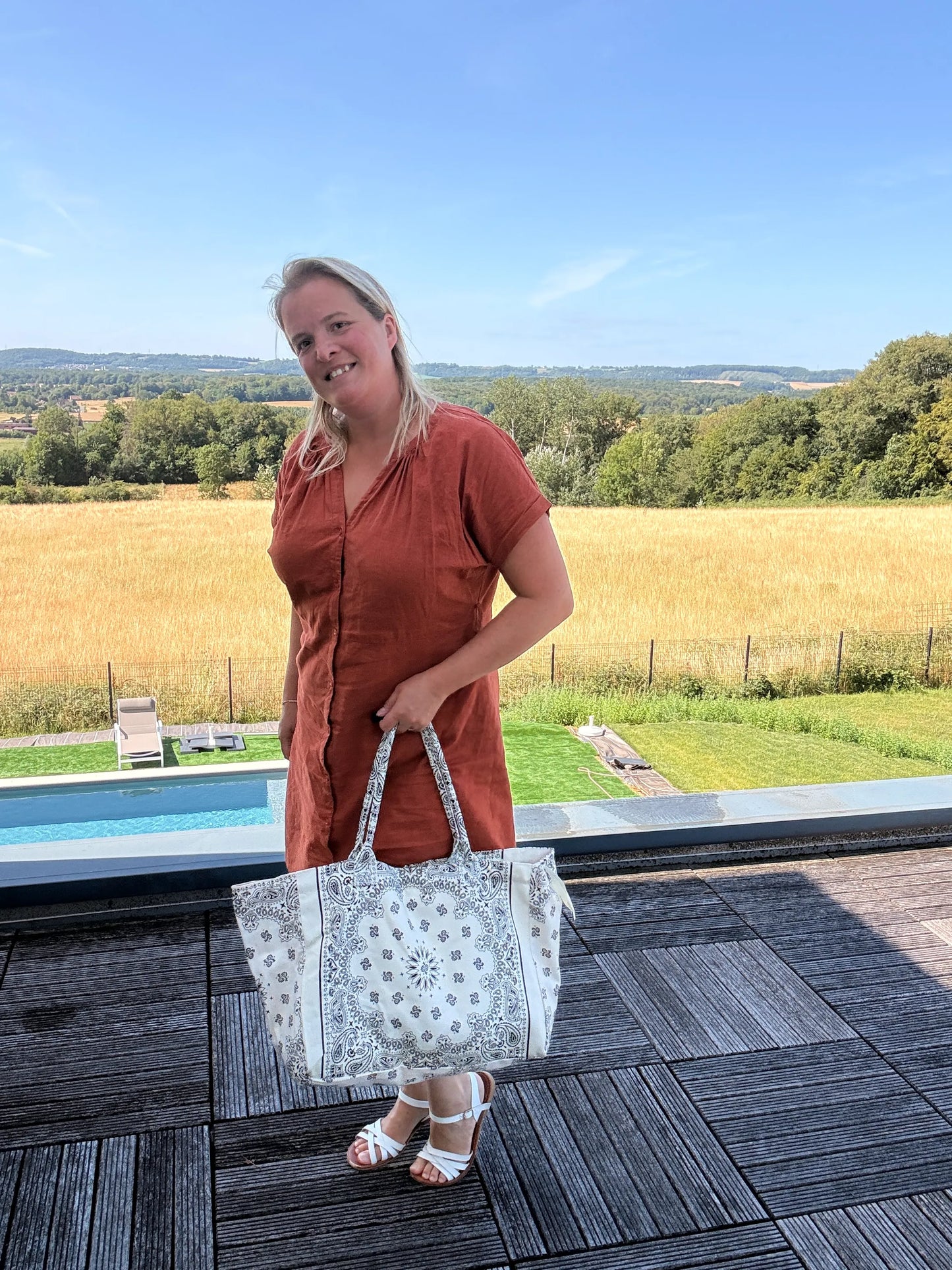 Grand sac polochon paisley blanc porté par une femme en robe orange, sur fond de campagne et piscine.