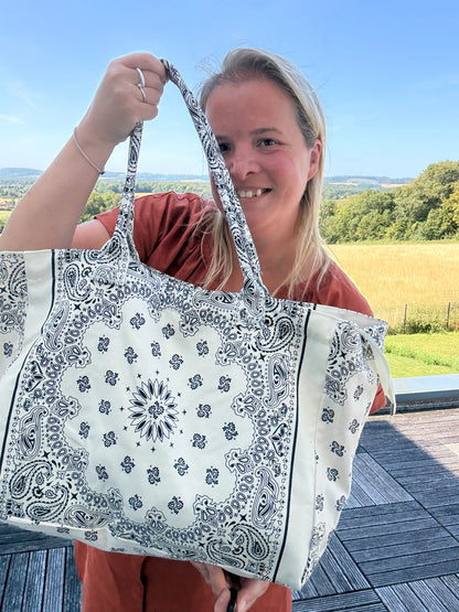 Grand sac polochon blanc à motif paisley bleu, porté par une femme sur fond champ et ciel, prêt à être emporté pour toutes les saisons.