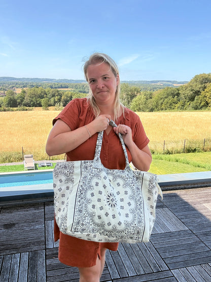 Homme ou femme portant un grand sac polochon blanc à motifs paisley, debout en extérieur près d’une piscine, paysage champêtre en arrière-plan. Grand Sac Polochon Paisley Blanc – Le Sac Bohème Chic de Toutes les Saisons.