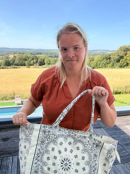 Sac polochon imprimé paisley blanc porté par une femme près d’une piscine, paysage champêtre en arrière-plan. Grand Sac Polochon Paisley Blanc – Le Sac Bohème chic.