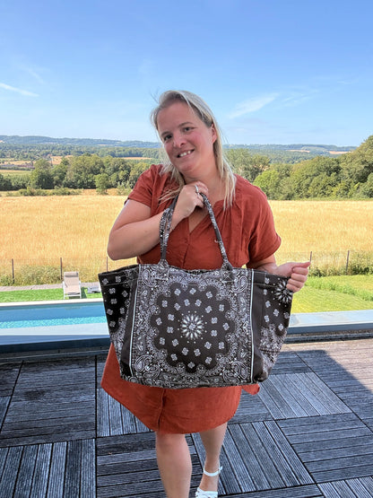 Grand sac polochon marron zippé porté par une femme sur une terrasse extérieure, paysage champêtre en arrière-plan.