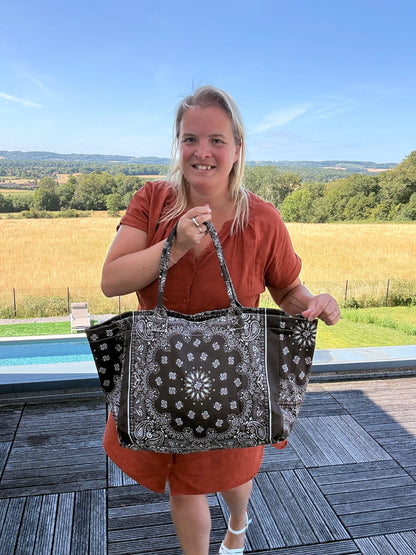 Homme ou femme tenant un grand sac polochon noir à motifs bandana, devant jardin et piscine.