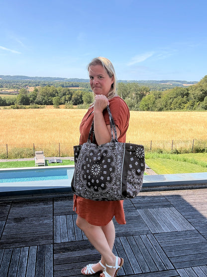 Grand sac polochon marron zippé porté par une femme près d’une piscine, campagne en arrière-plan, look chic et décontracté.