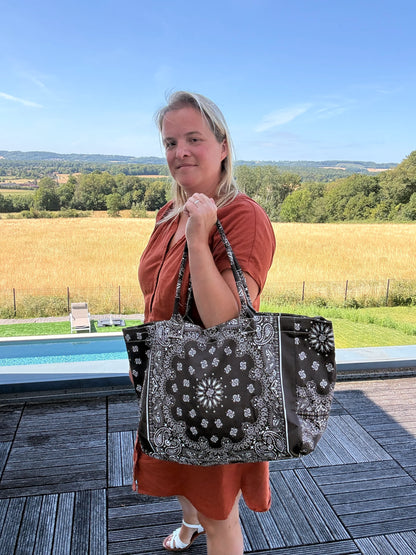Grand sac polochon marron zippé porté par une femme près d’une piscine, paysage rural en arrière-plan.