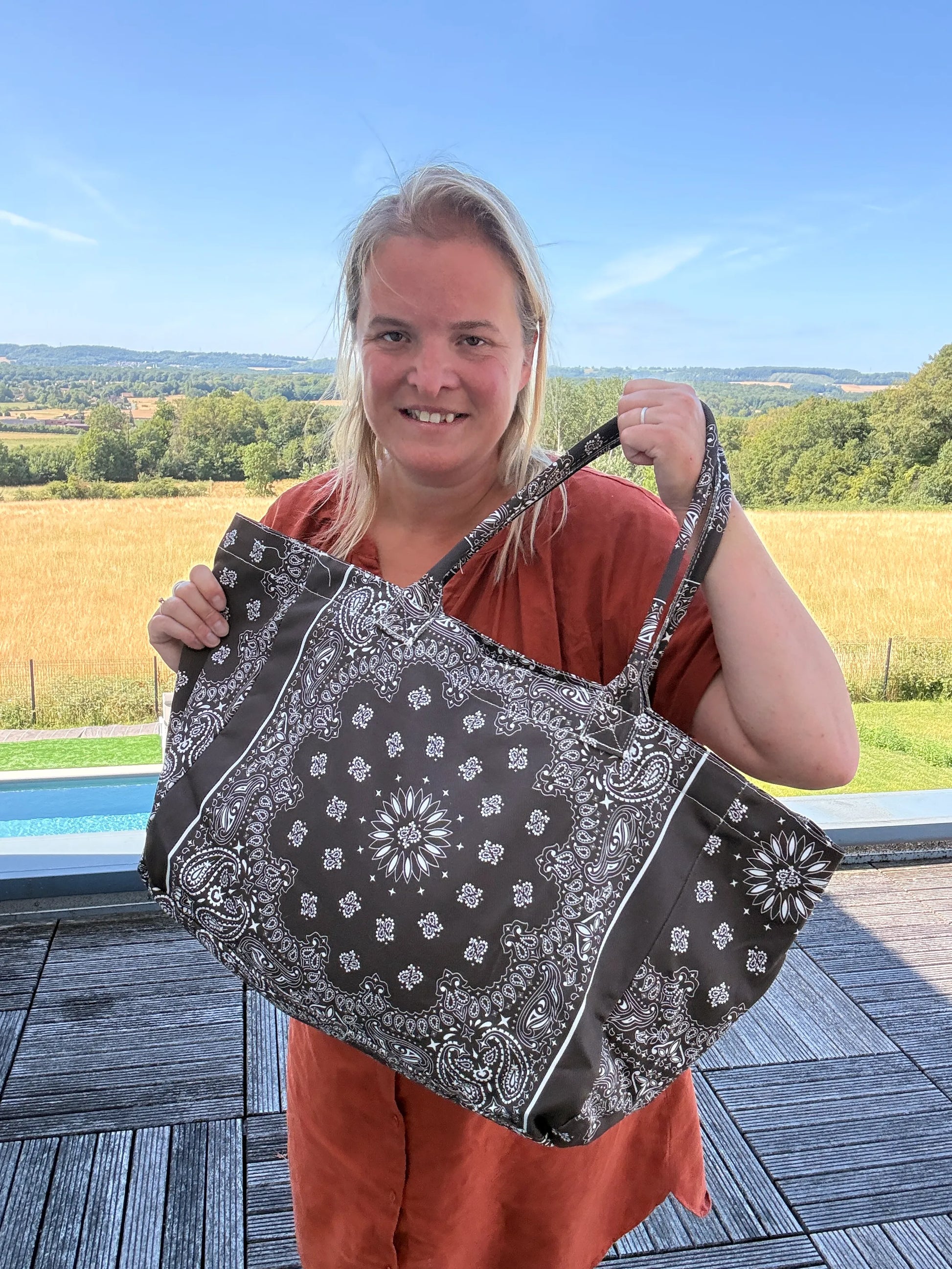 Grande sac polochon marron à motif bandana noir et blanc, porté par une femme en extérieur, prêt pour l’été.