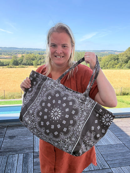 Grande sac polochon marron à motif bandana noir et blanc, porté par une femme en extérieur, prêt pour l’été.