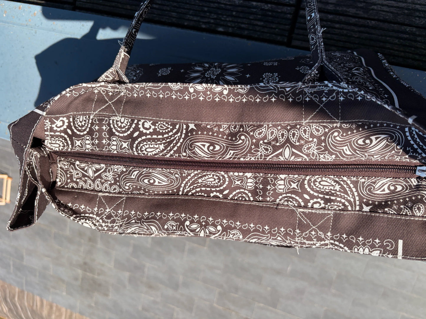 Grand sac polochon marron zippé avec motif bandana blanc, bords cousus, poches zippées et bandoulière; design stylé et spacieux.