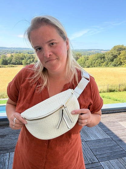 Sac banane Bohème femme en paille raphia beige avec bandoulière réglable, portée en extérieur près d’un paysage champêtre.