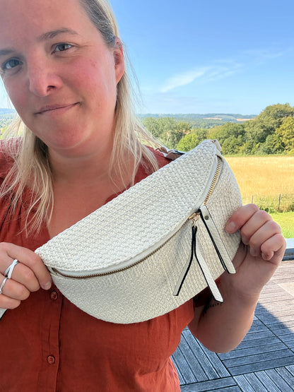 Sac banane bohème femme en paille raphia beige avec bandoulière réglable et fermeture zippée, portée près du corps.