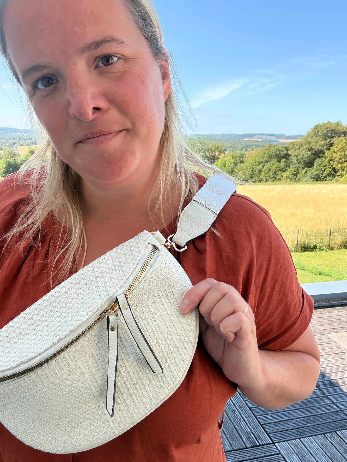 Sac banane bohème pour femme en paille raphia beige, portée en bandoulière réglable, avec fermeture zippée et détails dorés.