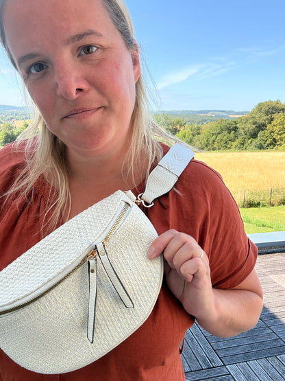 Sac banane bohème pour femme en paille raphia beige, portée en bandoulière réglable, avec fermeture zippée et détails dorés.