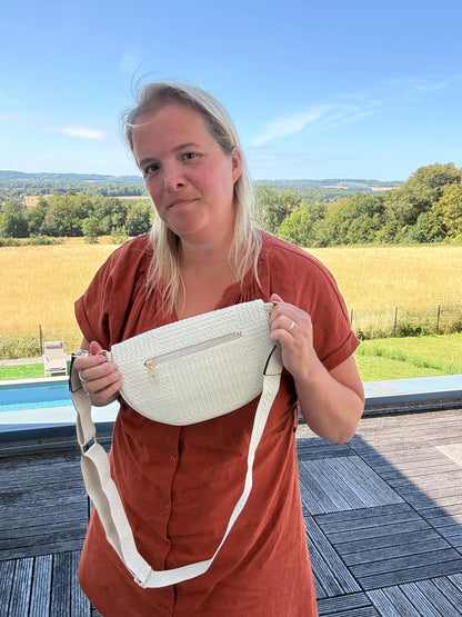 Sac banane Bohème femme en raphia beige avec bandoulière réglable portée par une femme, paysage champêtre en arrière-plan.