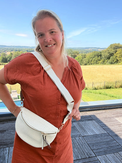 Sac banane bohème femme en paille raphia beige avec bandoulière réglable portée en diagonale sur l’épaule, près d’un terrain champêtre.
