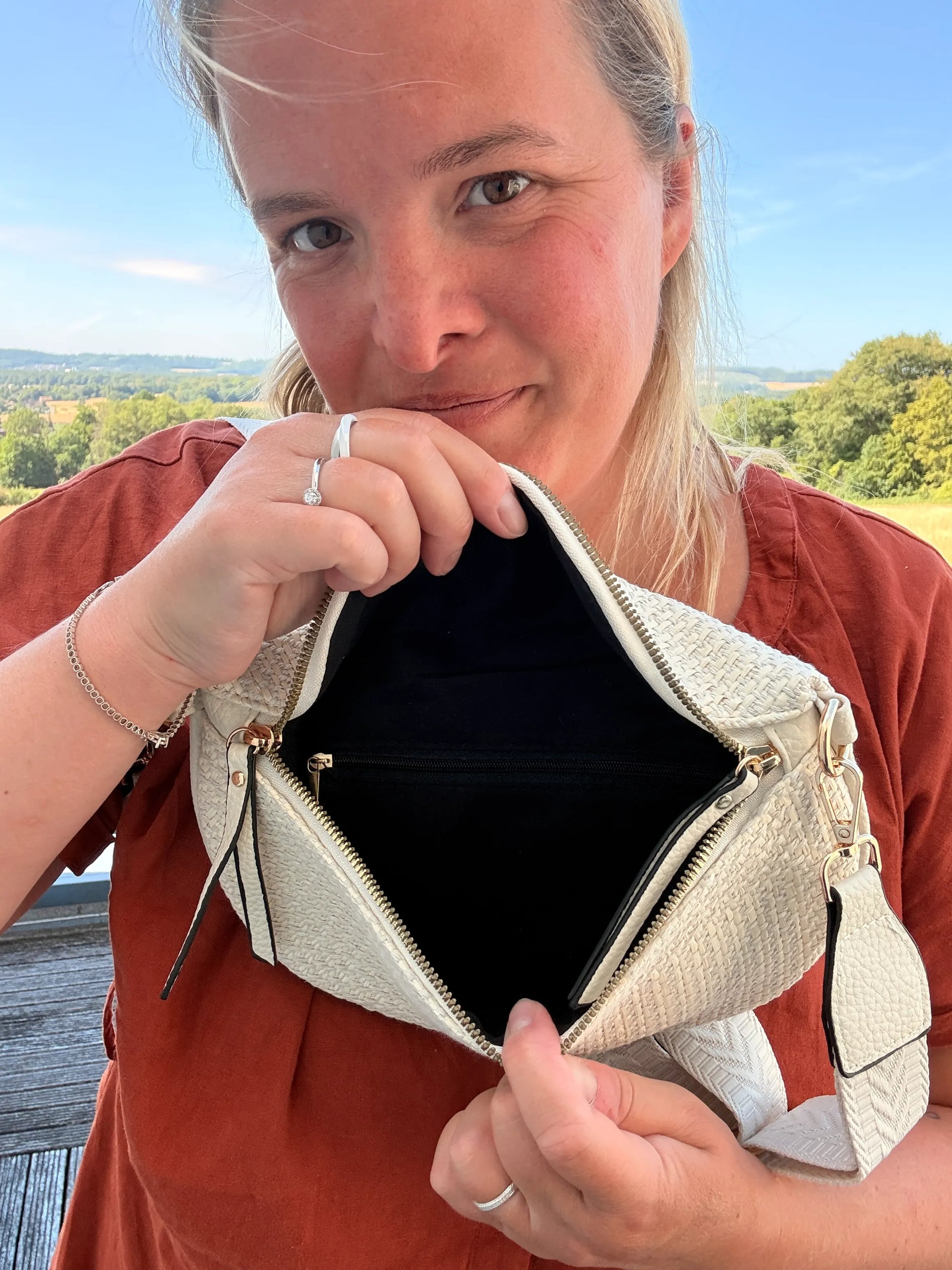 Sac Banane Bohème Femme : close-up d’une femme montrant l’intérieur beige clair et la poche zippée du sac en raphia, bandoulière réglable.