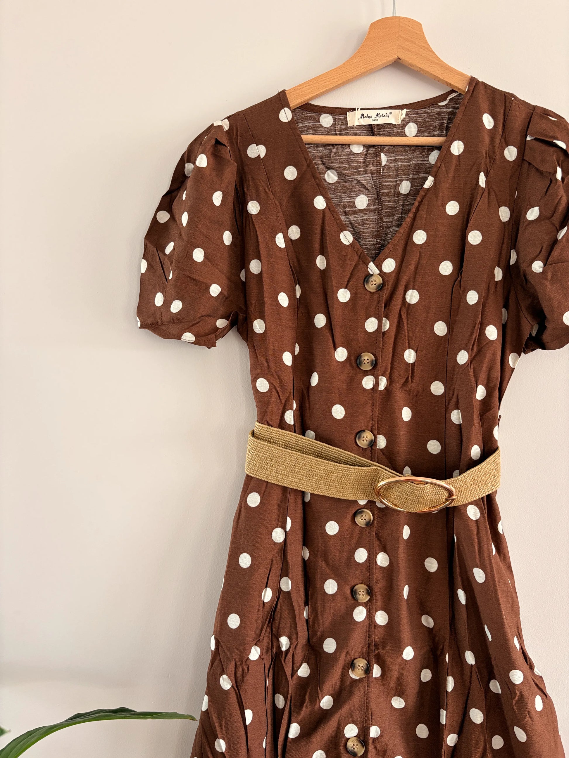 Robe midi à pois blancs sur fond beige-brun avec manches bouffantes, col en V et ceinture ceinturant la taille.