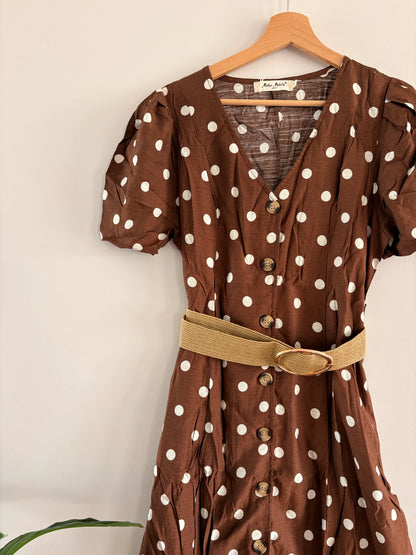 Robe midi à pois blancs sur fond beige-brun avec manches bouffantes, col en V et ceinture ceinturant la taille.