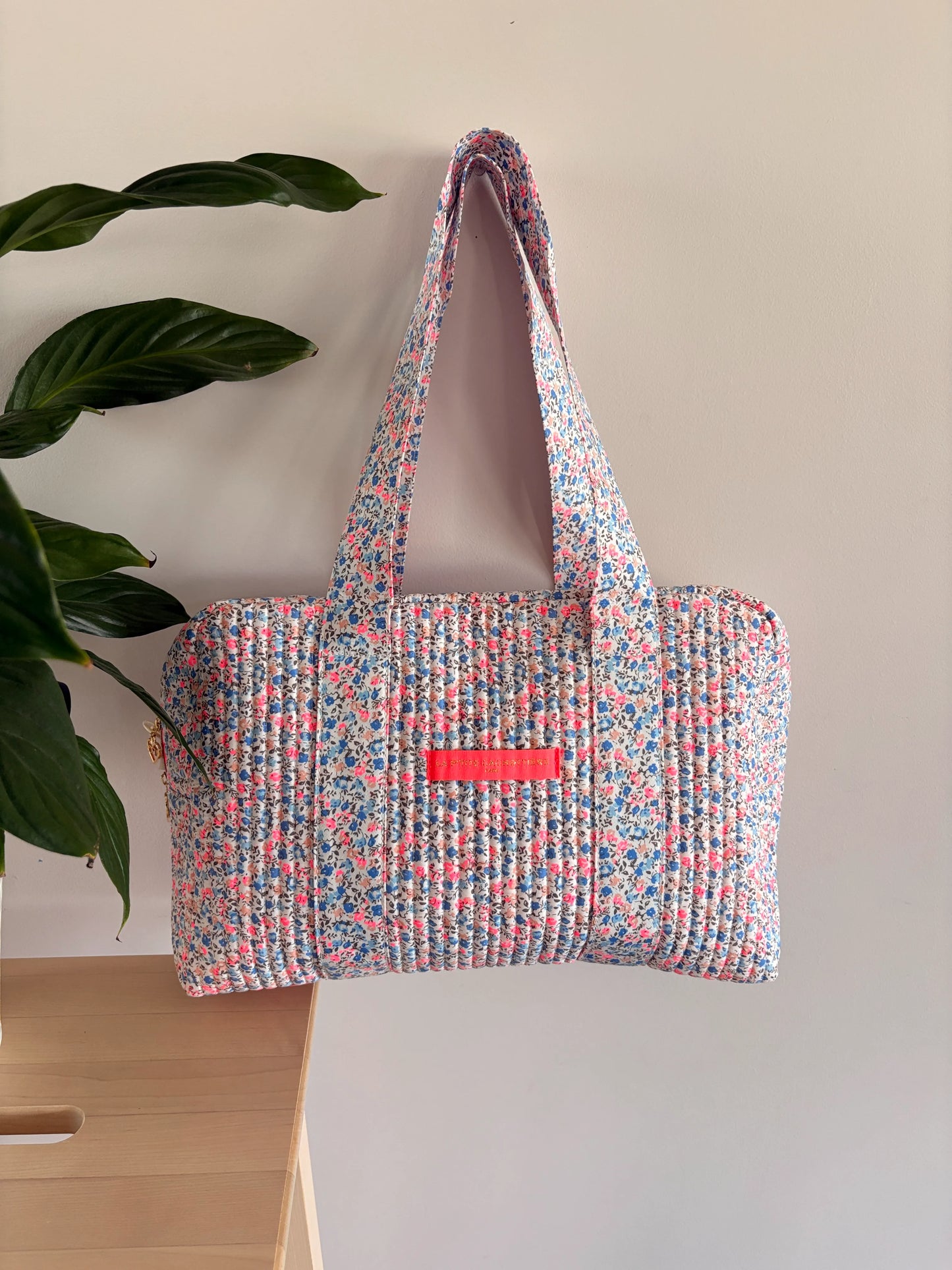 Sac polochon matelassé à imprimé liberty lilas, rose et bleu, avec poignée et poche frontale rose vif.