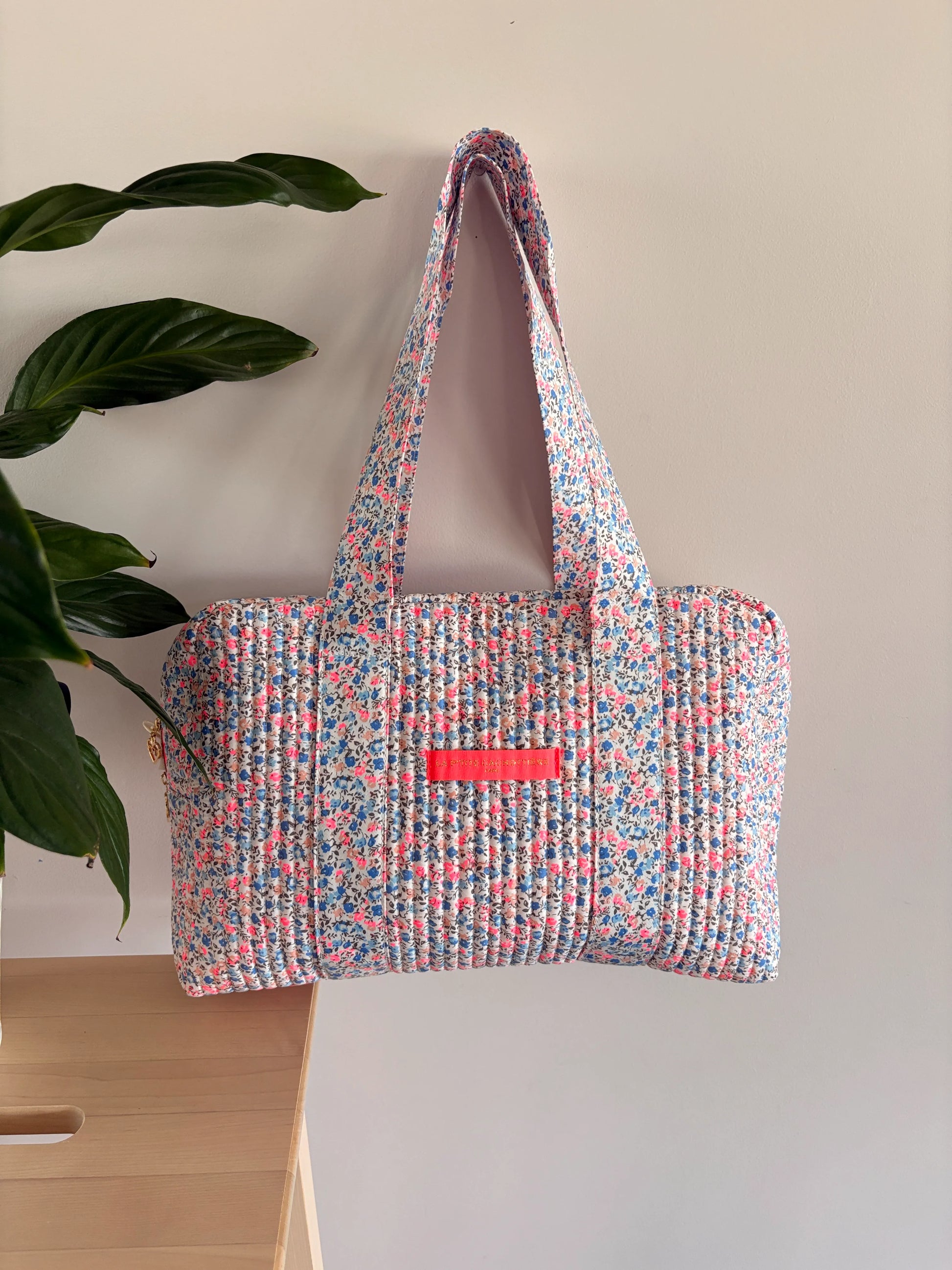 Sac polochon matelassé à imprimé liberty lilas, rose et bleu, avec poignée et poche frontale rose vif.
