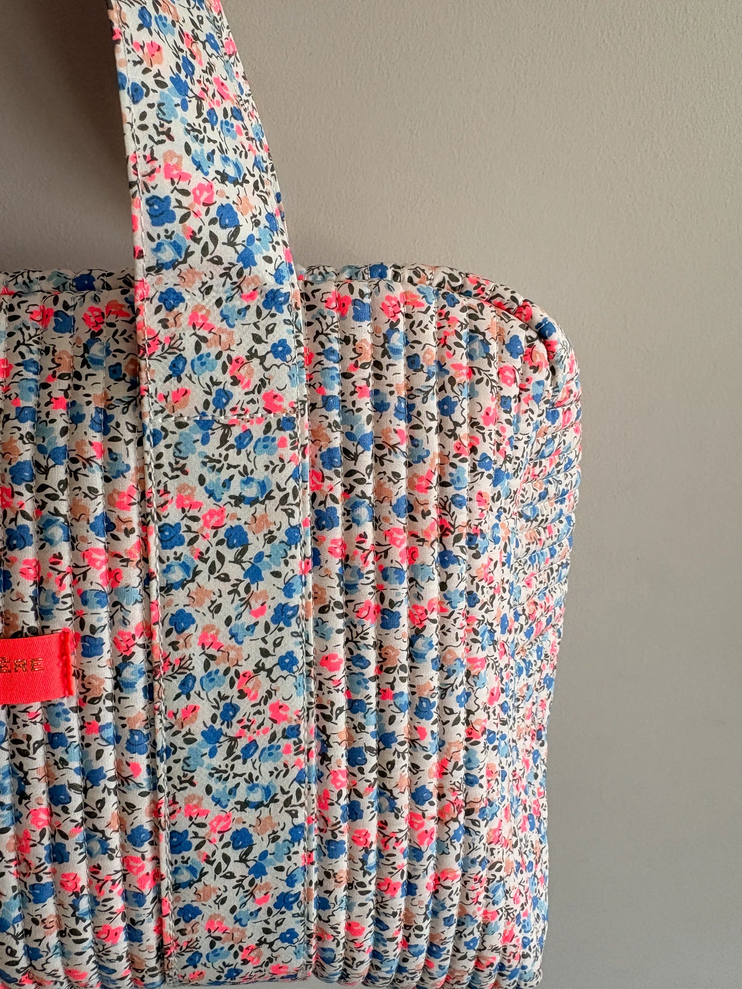 Sac polochon matelassé fleurie imprimé Liberty lilas, rose et bleu, poignée rembourrée et fermeture zippée visible.