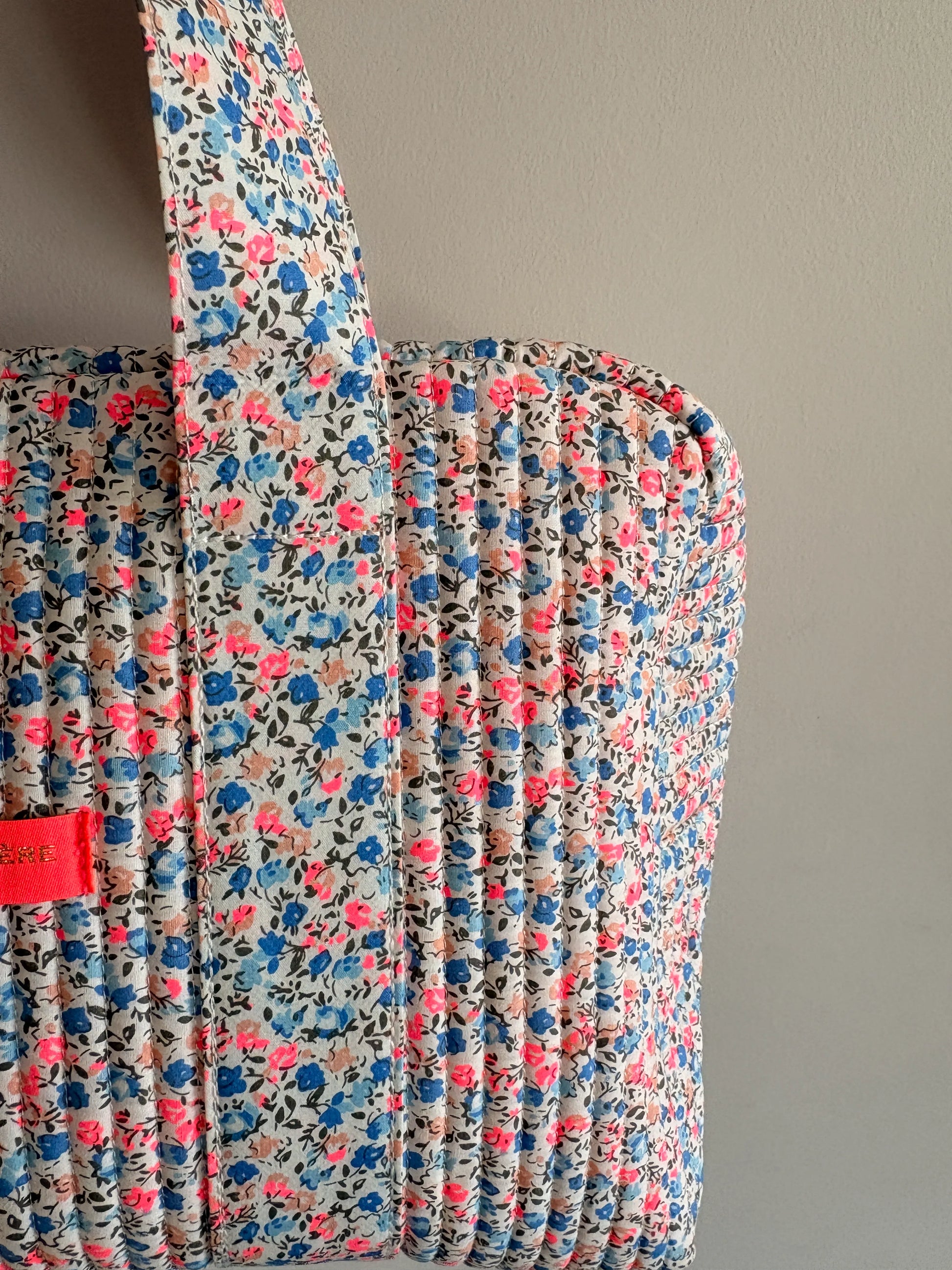Sac polochon matelassé fleurie imprimé Liberty lilas, rose et bleu, poignée rembourrée et fermeture zippée visible.