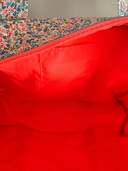 Sac polochon matelassé floral avec doublure intérieure rouge vif et poche latérale visible.