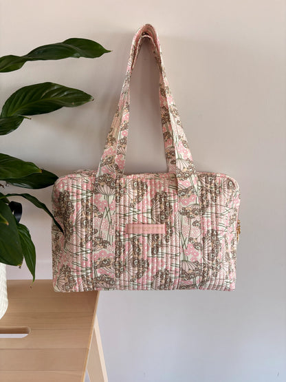 Sac polochon matelassé rose fleuri, bagage cabine chic à deux poignées, prêt pour voyage femme.