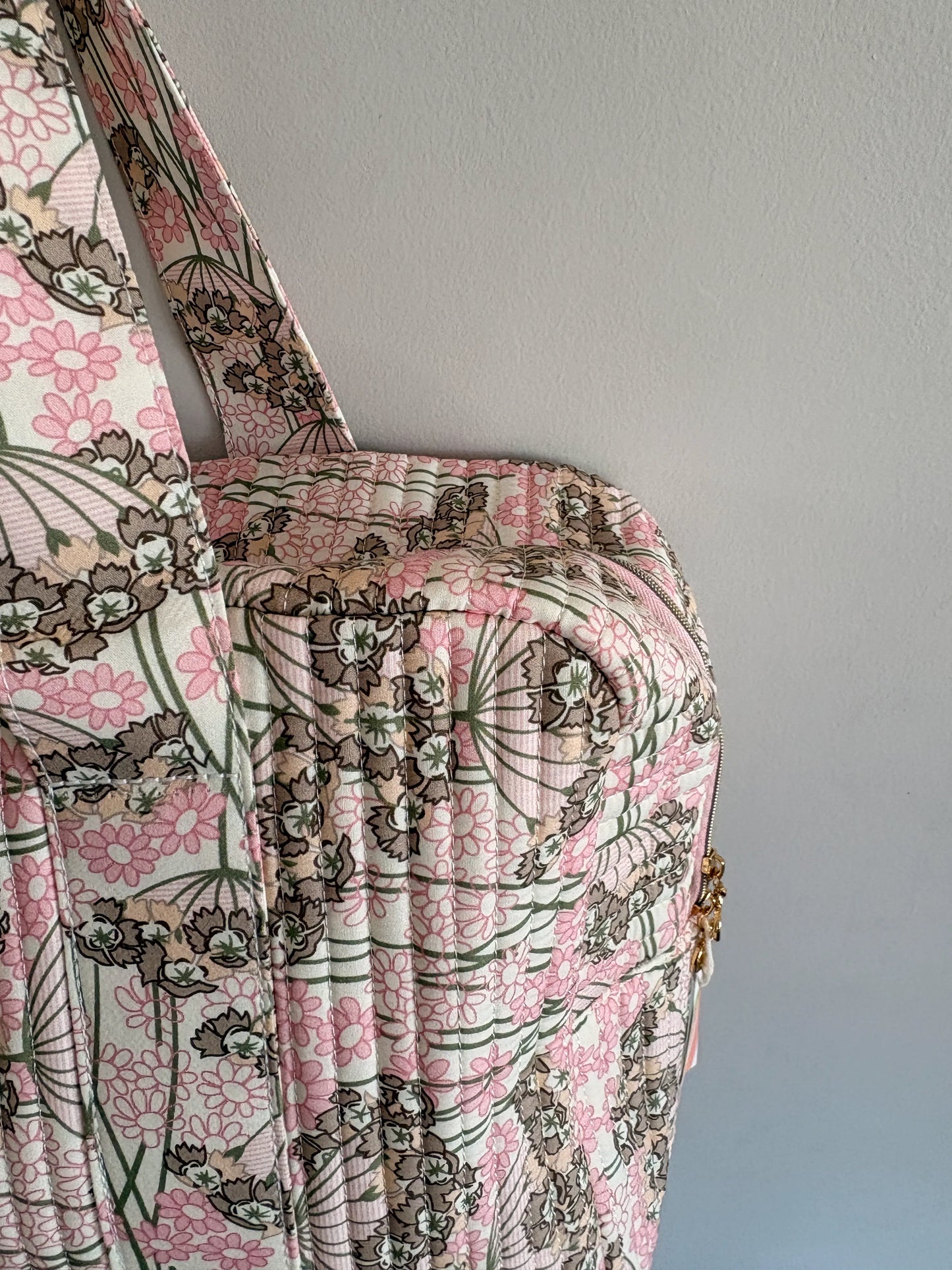 Sac polochon matelassé rose fleuri, style bagage cabine femme avec motif floral et fermeture dorée visible.