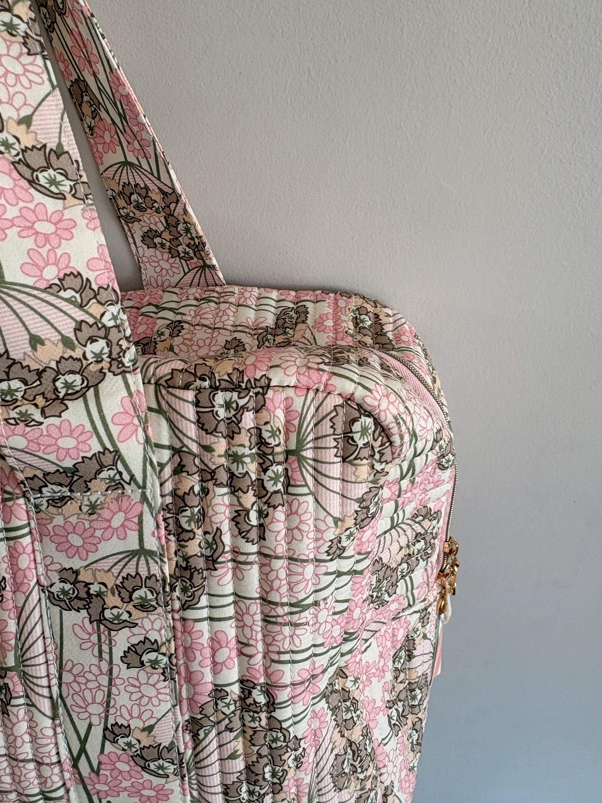 Sac polochon matelassé rose fleuri, style bagage cabine femme avec motif floral et fermeture dorée visible.