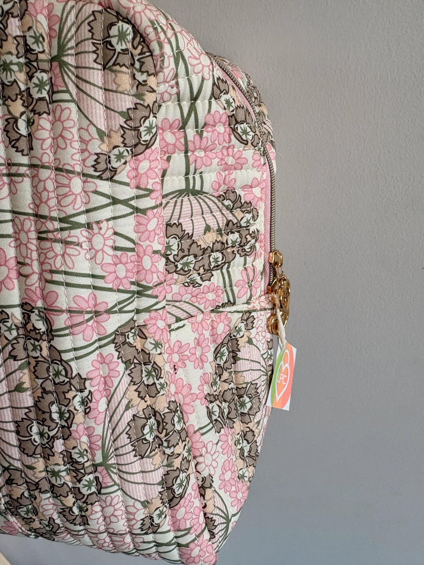 Sac polochon matelassé rose fleuri avec motif floral, cadenas doré et étiquette, prêt pour voyage cabine.