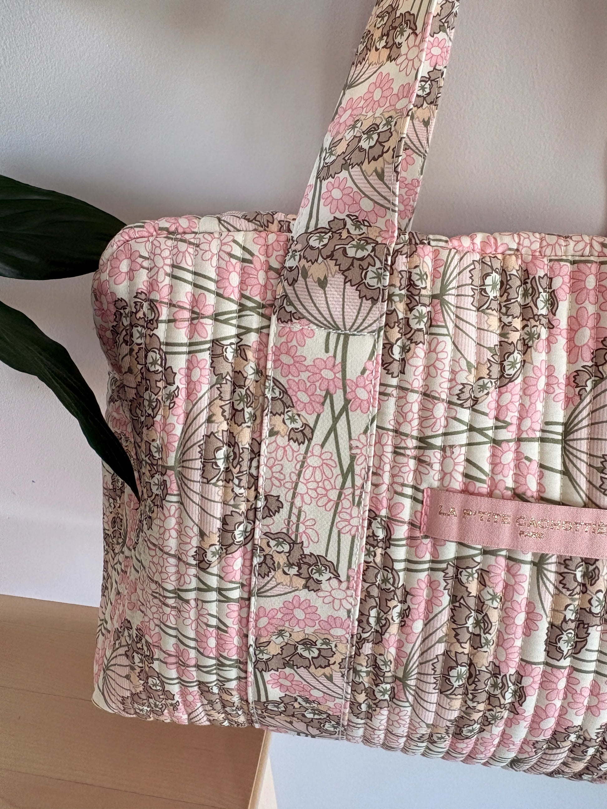 Sac polochon matelassé rose fleuri avec poignée; motif floral et cuirette rose clair, étiquette “SAC CAM?.” (Nom produit à intégrer: Sac Polochon Matelassé Rose Fleuri – Bagage Cabine & Sac de Voyage Femme)