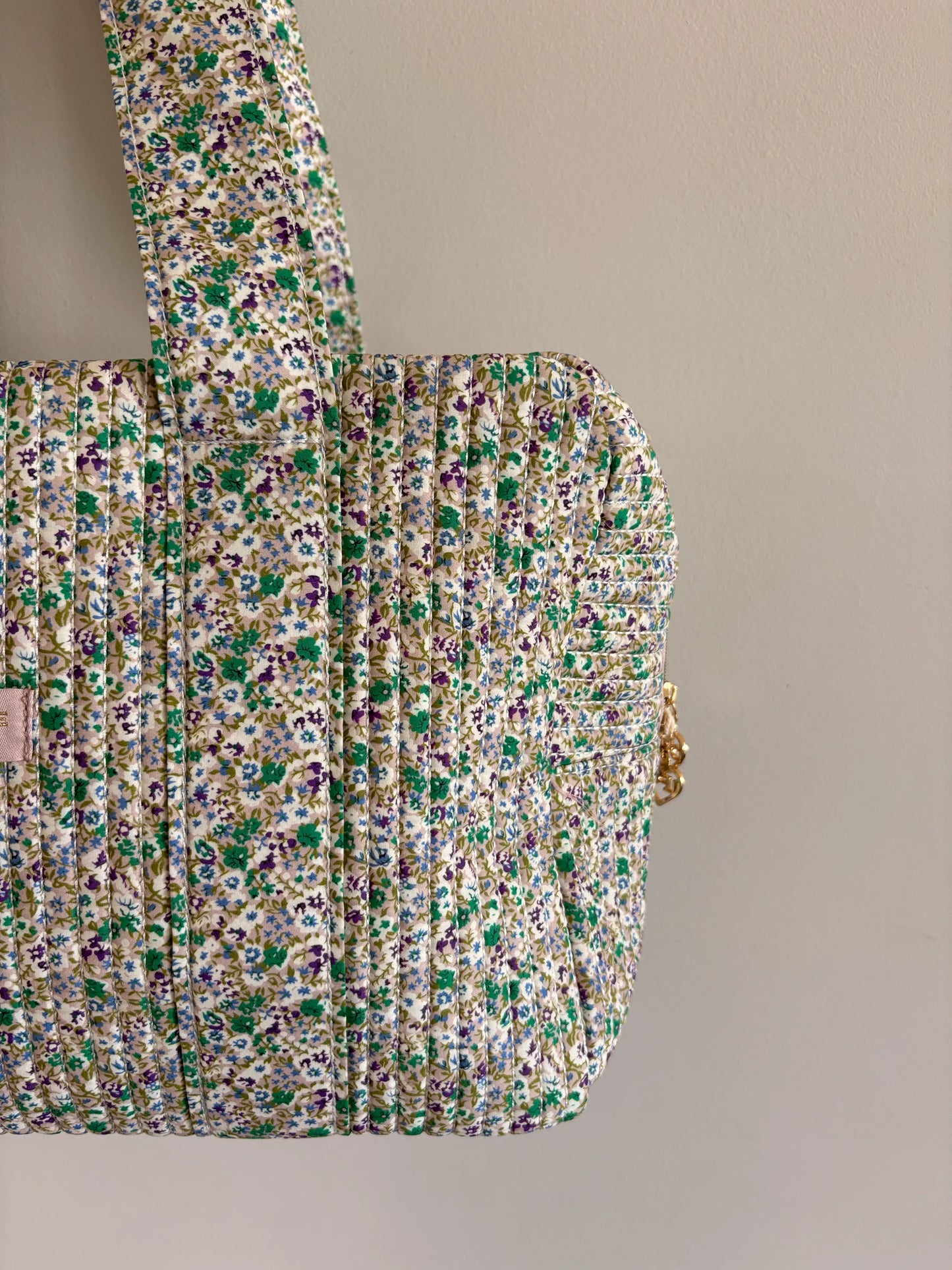Sac polochon vert à motif floral, matelassé, avec bandoulière et fermeture dorée, côté porté sur fond neutre.