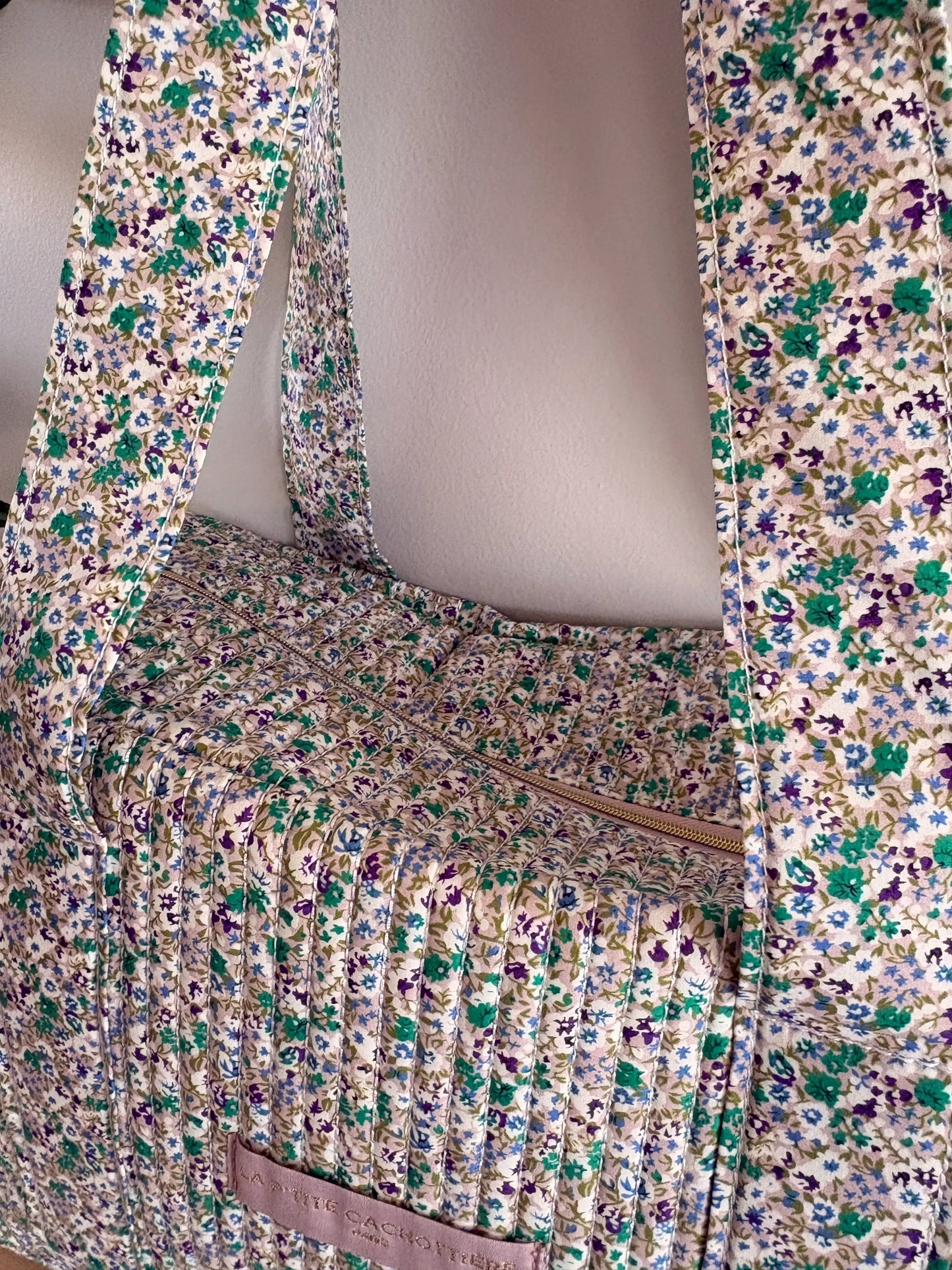 Sac polochon vert à motif floral et matelassé, avec sangles et poche zippée sur le dessus.
