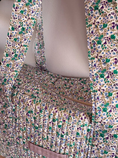 Sac polochon vert à motif floral et matelassé, avec sangles et poche zippée sur le dessus.