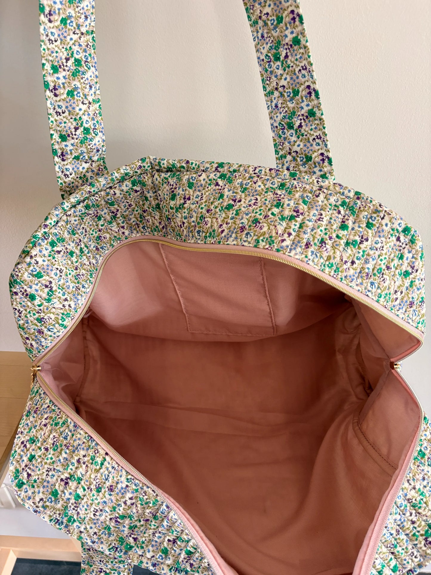 Sac polochon vert à motif floral avec intérieur rose et bijoux de fermeture, prêt à voyager.