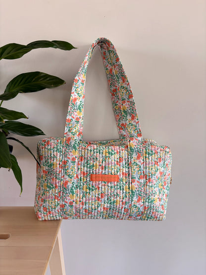 Sac polochon matelassé fleuri vert menthe, imprimé fleurs, avec anses WE longilignes et pochette orange sur le devant.