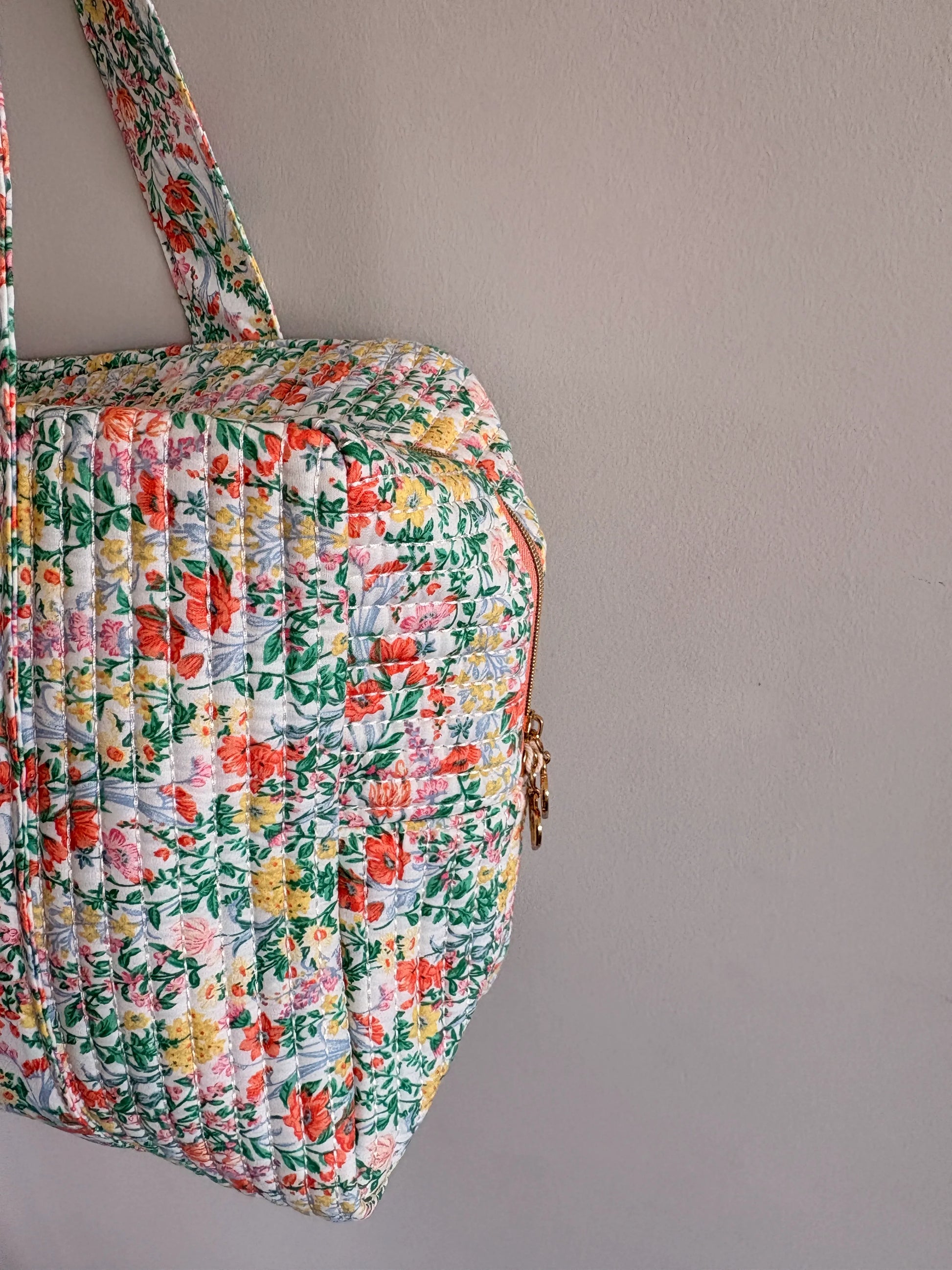 Sac polochon matelassé imprimé fleurs vert menthe porté sur fond neutre, motif floral multicolore et fermeture éclair dorée.