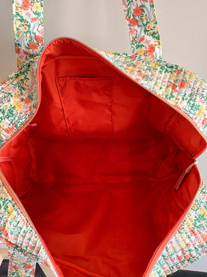 Sac polochon matelassé imprimé fleurs femme, intérieur rouge vif avec poche zippée et doublure assortie.