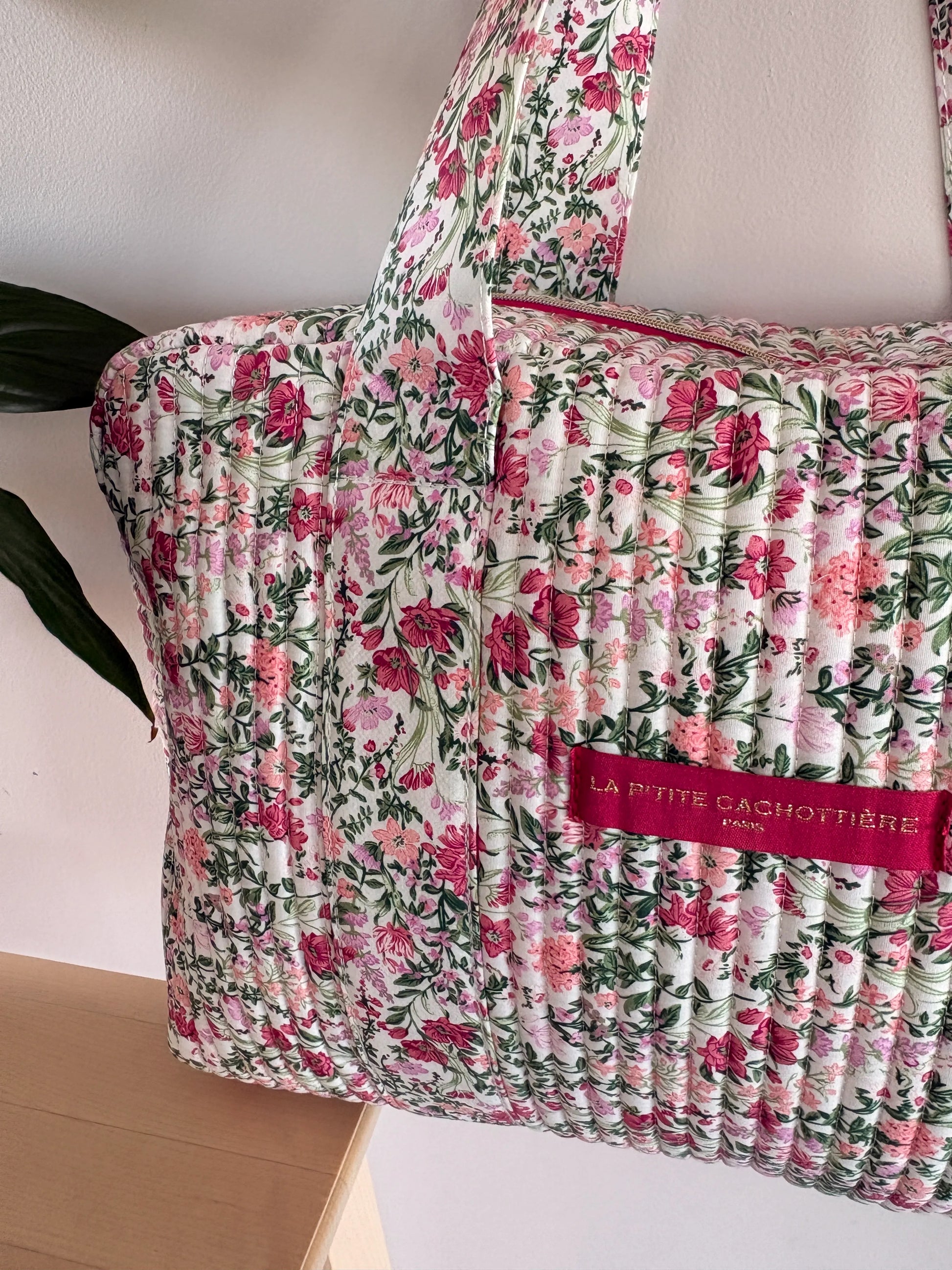 Sac polochon matelassé à motif floral rose pivoine et vert sauge sur fond blanc, avec poignée et étiquette rose clair.