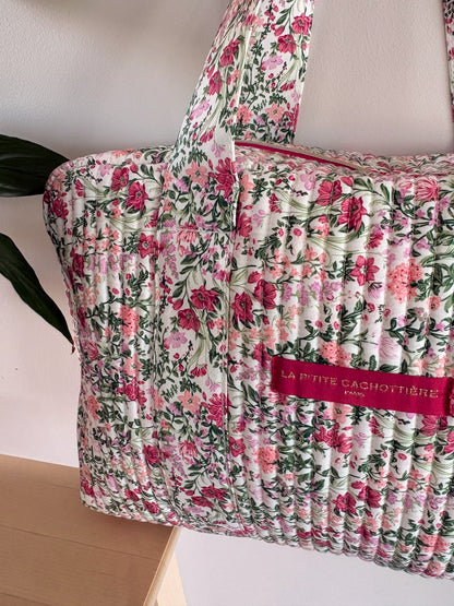 Sac polochon matelassé à motif floral rose pivoine et vert sauge sur fond blanc, avec poignée et étiquette rose clair.