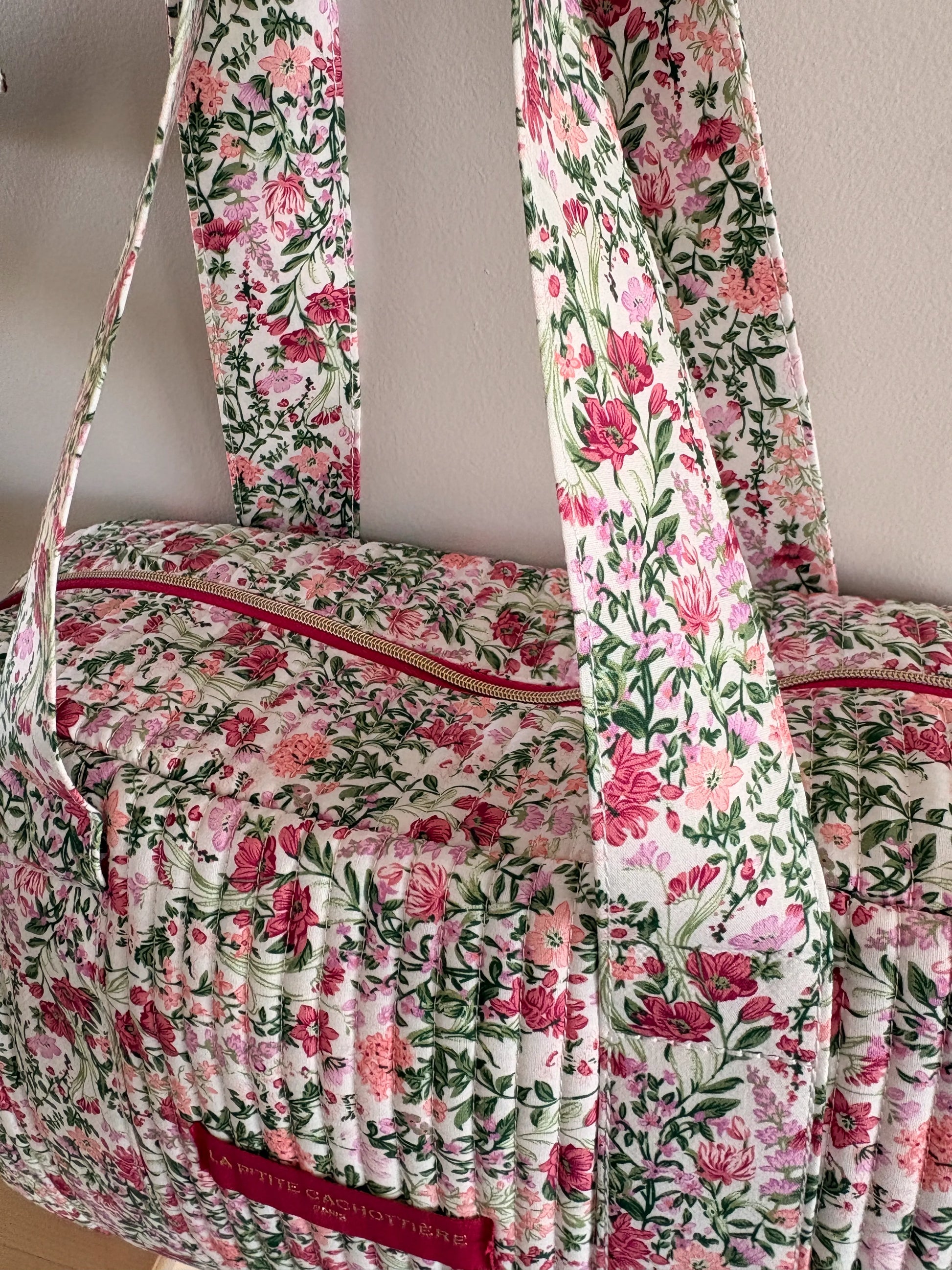 Sac polochon matelassé floral rose et vert avec fond blanc, imprimé fleurs roses et feuillage, bandoulière et poches zippées.