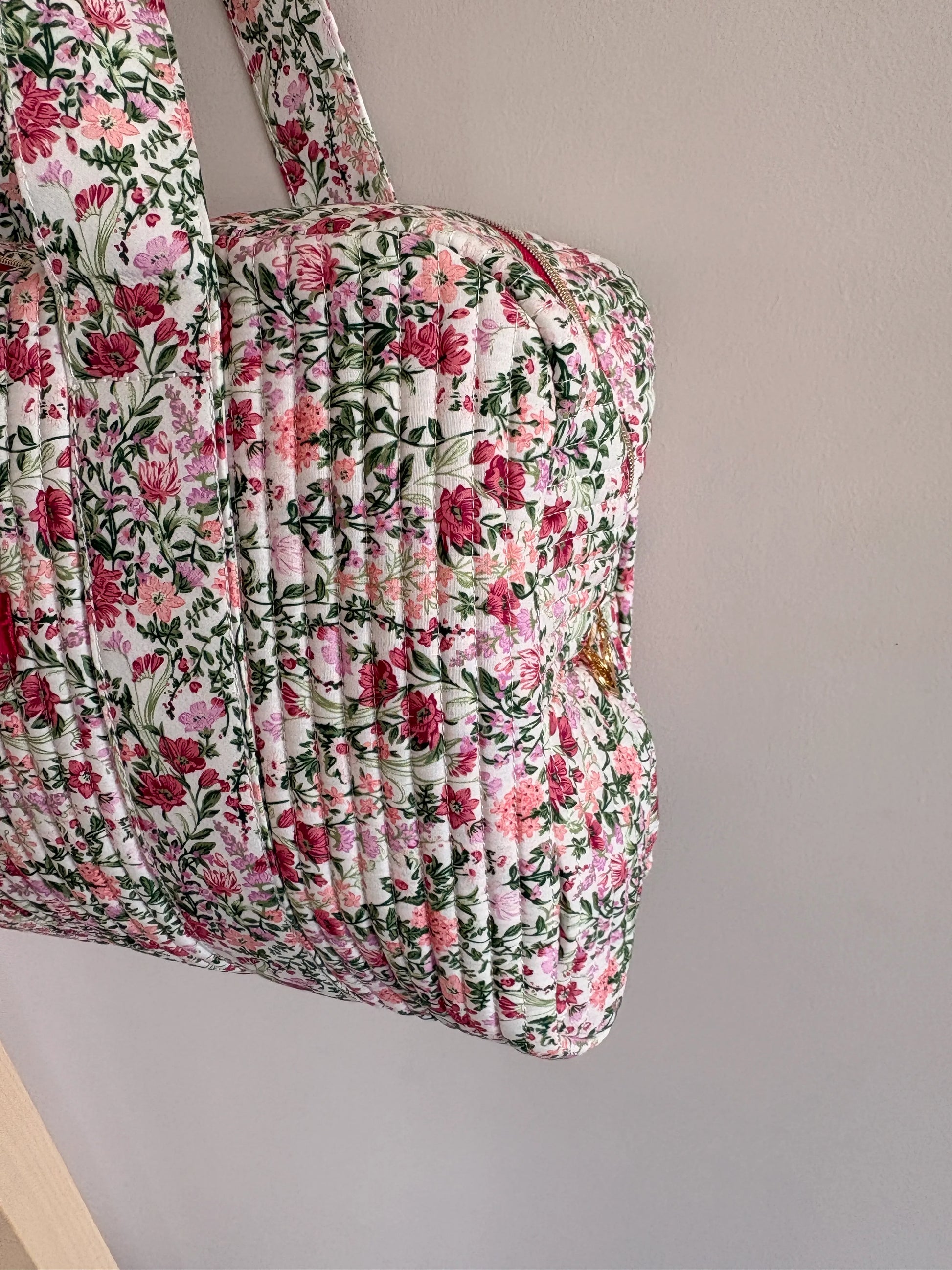 Sac polochon matelassé fleurs rose et vert sauge sur fond blanc, motif floral dense.