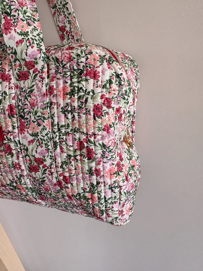 Sac polochon matelassé fleurs rose et vert sauge sur fond blanc, motif floral dense.
