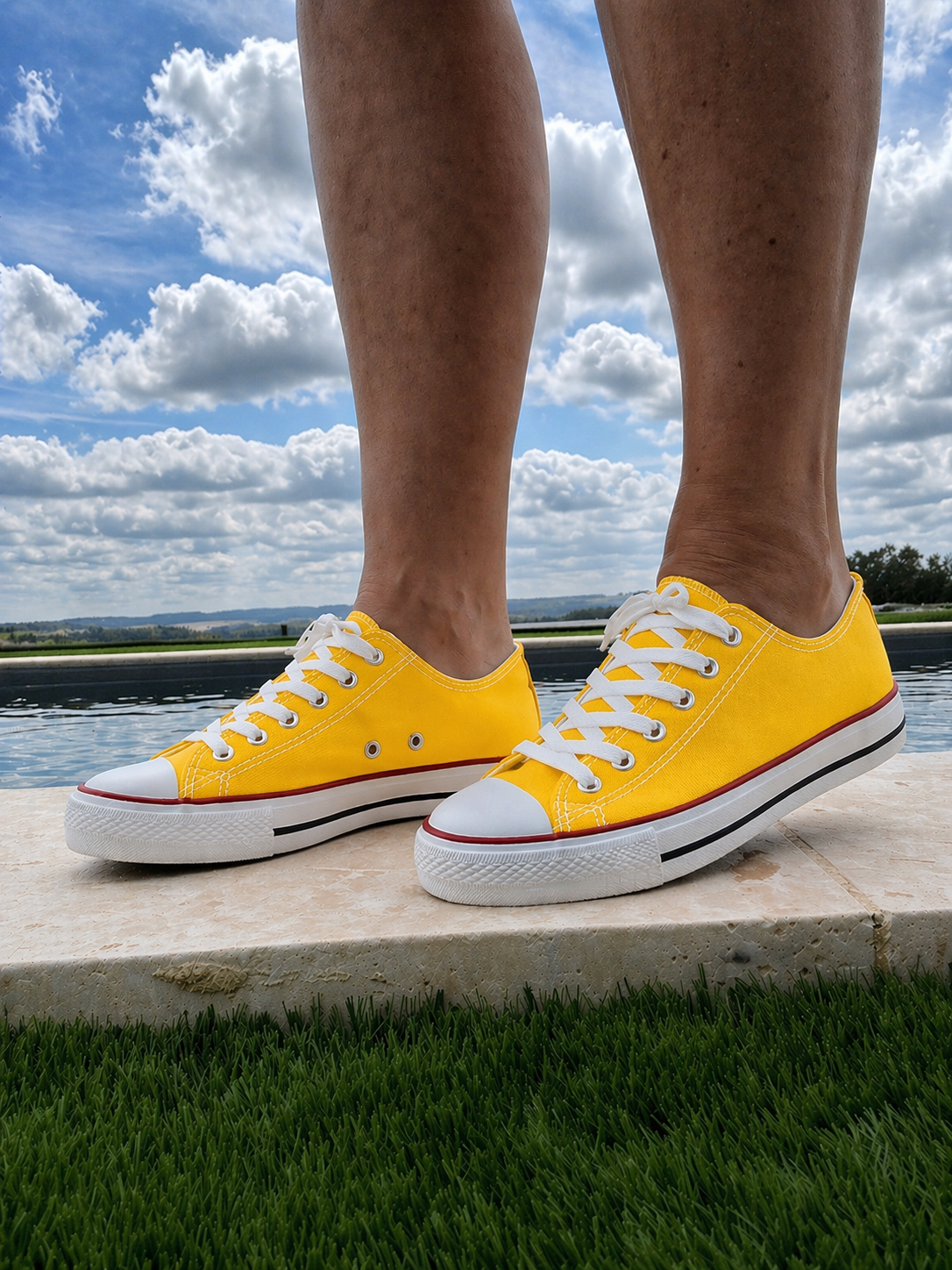 Converse jaunes à lacets blanches portée par une personne debout près d’un plan d’eau, sous un ciel nuageux.